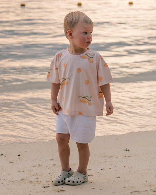 Child on the beach at sunset wearing Wildgreen’s Apricot T-shirt from the Island Life collection. Made from 100% GOTS-certified organic cotton, this unisex kids tee features a soft apricot-hued print, perfect for eco-conscious families seeking sustainable and stylish clothing. #OrganicKidswear #SustainableFashion