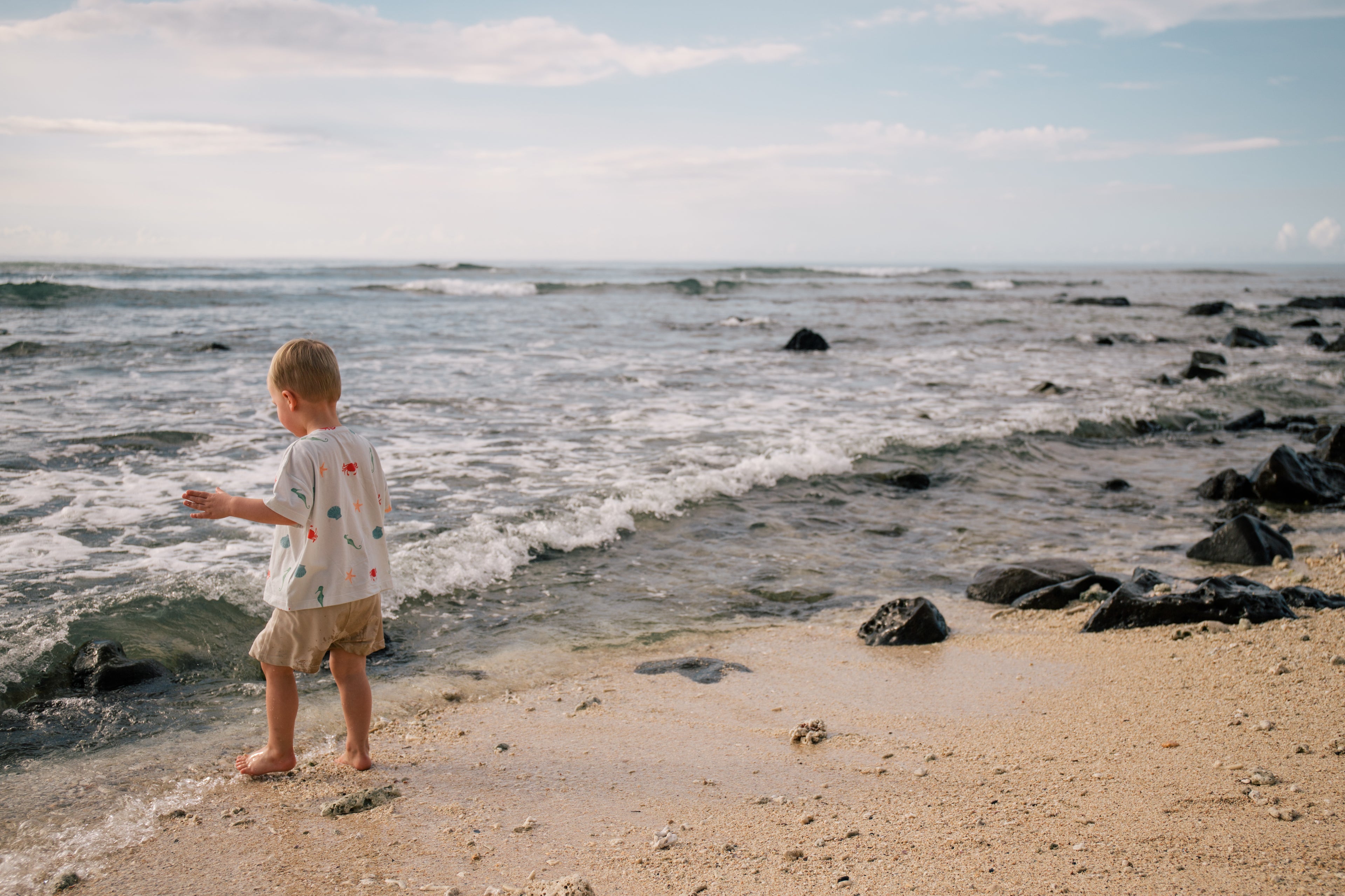Toddler wearing Wildgreen’s Marine T-shirt, crafted from 100% GOTS-certified organic cotton, playing on a tropical beach. This gender-neutral, ocean-inspired kidswear piece is soft, breathable, and perfect for eco-conscious families who love adventure. #OrganicKidswear #SustainableFashion #BeachStyle