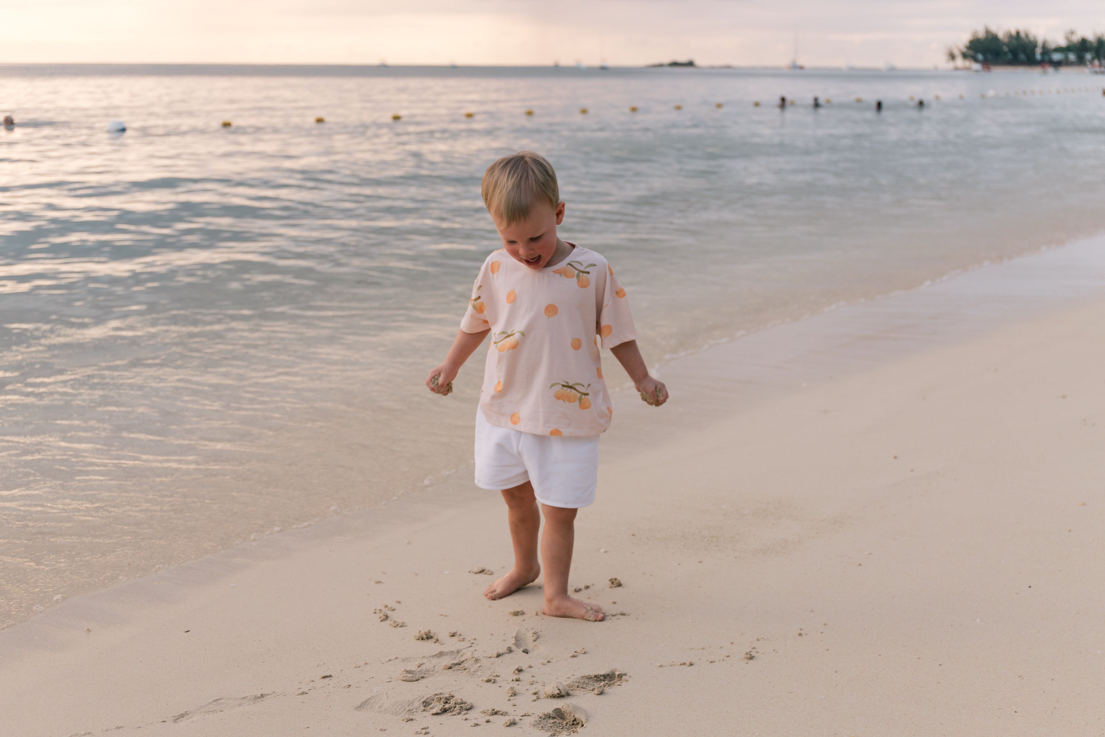 Toddler wearing Wildgreen’s Apricot T-shirt, made from 100% GOTS-certified organic cotton, exploring the beach at sunset. This gender-neutral, sustainable kidswear piece is perfect for nature-loving families seeking stylish and eco-conscious clothing. #OrganicKidswear #SustainableFashion #BeachStyle