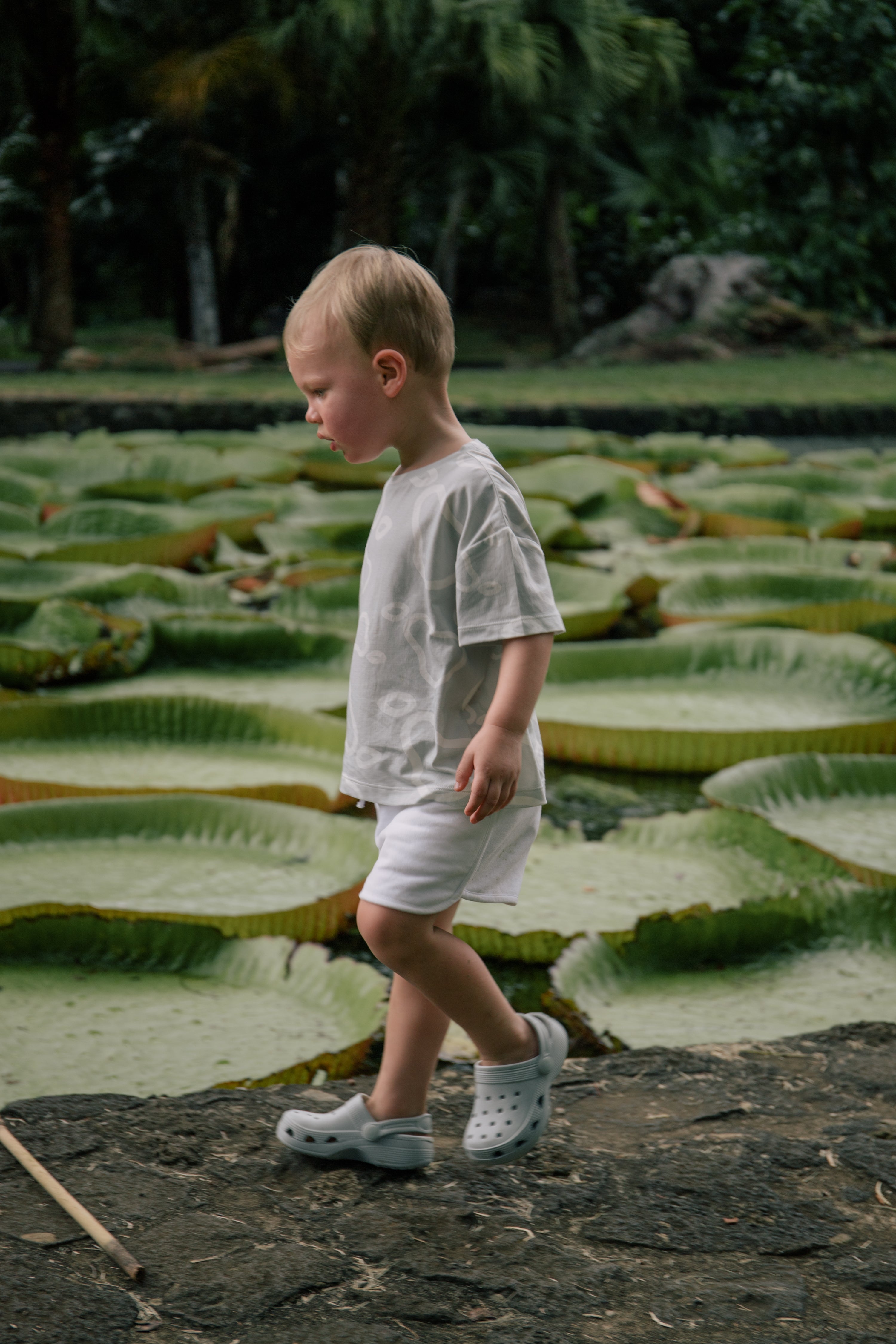 Toddler wearing Wildgreen’s White Pear T-shirt, made from 100% GOTS-certified organic cotton, standing by a serene lily pad pond. This gender-neutral, sustainable kidswear piece blends comfort and eco-conscious style, perfect for little explorers. #OrganicKidswear #SustainableFashion #NatureInspiredFashion